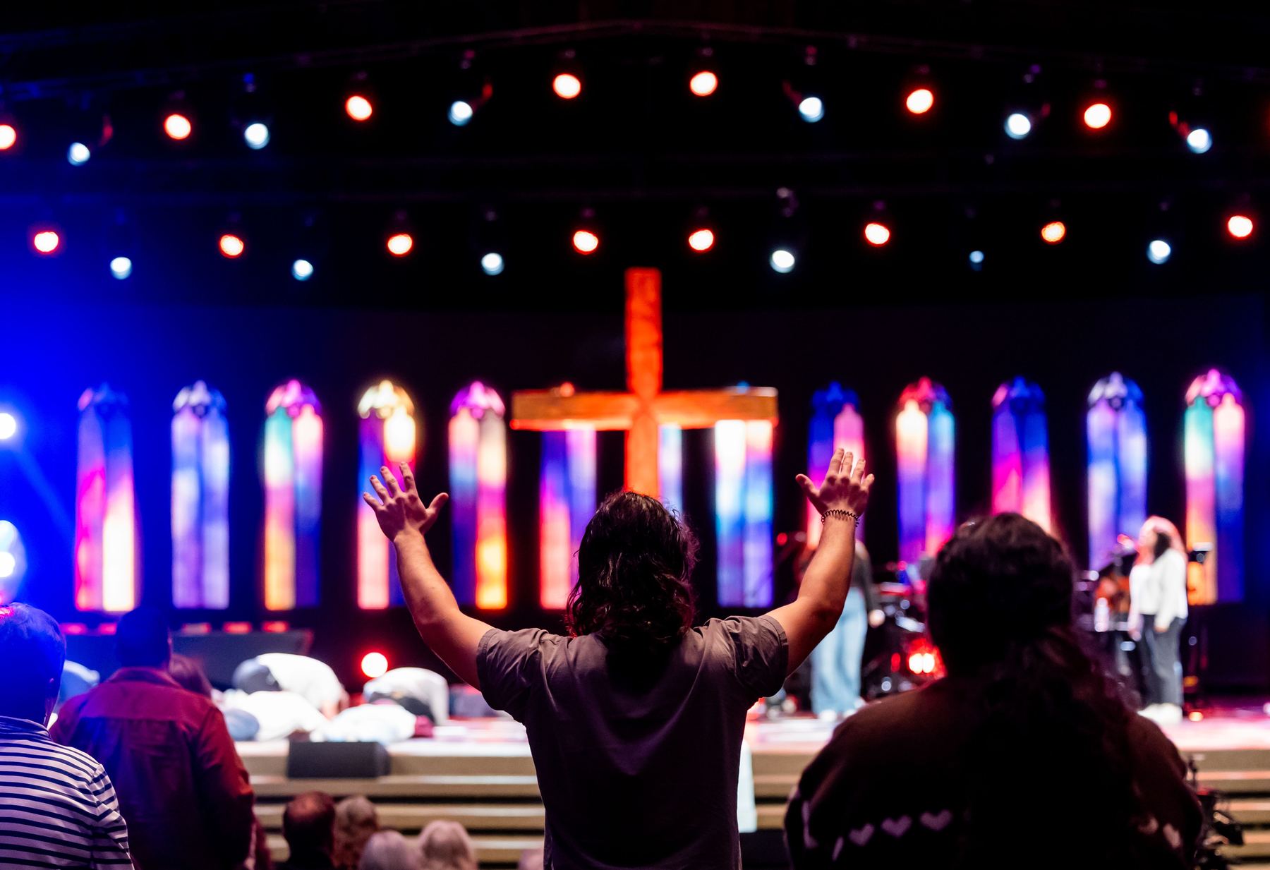 Members of the congregation singing and raising hands in worship, stained glass and a wooden cross behind them